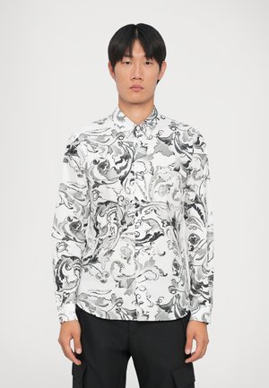 Chemise blanche ornée de motifs abstraits en noir, col boutonné, à manches longues et avec des détails textuels subtils sur l'épaule.