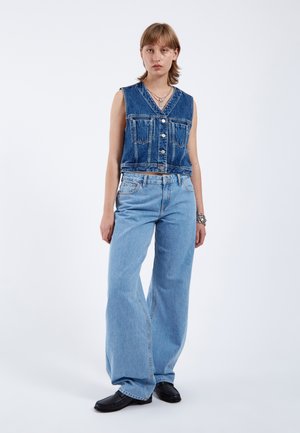 Denim vest with buttons and pockets paired with light blue wide-leg jeans. Both feature a classic denim texture and color.