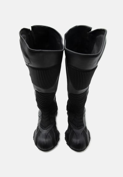 Ψηλές μαύρες μπότες με υφασμάτινη υφή με ρίγες και λαστιχένιες σόλες, φαίνονται από πάνω σε λευκό φόντο.
