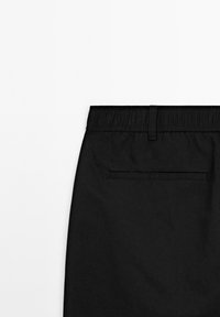 Back view of black pants featuring an elastic waistband, belt loop, and a single welt pocket on a white background.
