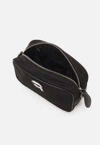Borsa in nylon nero con chiusura a zip e accento in logo argentato. L'interno presenta una fodera a motivo. Forma sottile e rettangolare.