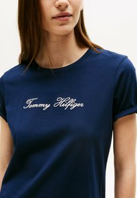 Mørkeblå bomulds t-shirt med rund halsudskæring og oprullede ærmer, med hvid broderet "Tommy Hilfiger" tekst på fronten.