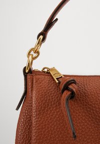 Bolsa de mão em couro castanho com um acabamento texturizado, hardware em tom de ouro e um detalhe de couro torcido no fecho de zíper.
