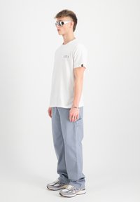 Camiseta de algodón blanca con el logo "HALF A" en colores; pantalones cargo gris claro; gafas de sol reflectantes; zapatillas New Balance.