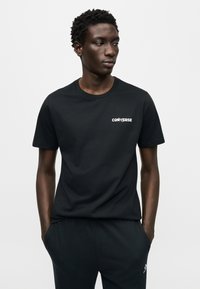 Μαύρο βαμβακερό t-shirt με κοντά μανίκια, στρογγυλή λαιμόκοψη και λευκό λογότυπο "CONVERSE" στο αριστερό στήθος. Λείο υφές και κανονική εφαρμογή.