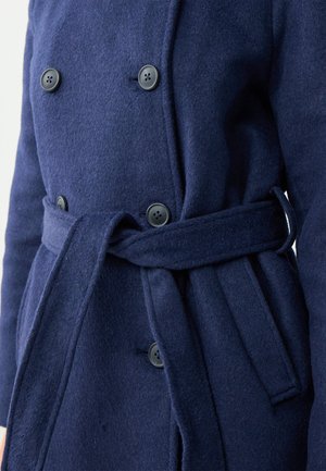 Cappotto in misto lana blu navy con design doppiopetto, bottoni neri, cintura da annodare e una texture morbida. Accentuato da dettagli cuciti.