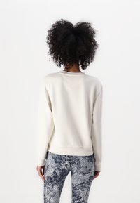 Creme-kleurig sweatshirt met een ronde hals en ribbelachtige zoom, gecombineerd met blauwe leggings met bloemenpatroon, waarbij de zachte texturen en comfort worden benadrukt.