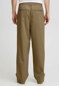 Bruine, wijde broek met een gestructureerde afwerking, voorzien van een rekbare tailleband en twee achterzakken, gezien vanuit de achterzijde.