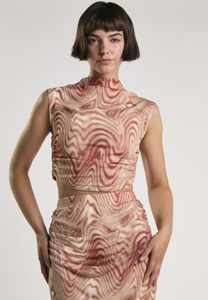 Kobieta o krótkich ciemnych włosach, ubrana w bezrękawowy krótki top z wysokim dekoltem i pasującą spódnicę w falisty czerwono-beżowy wzór.