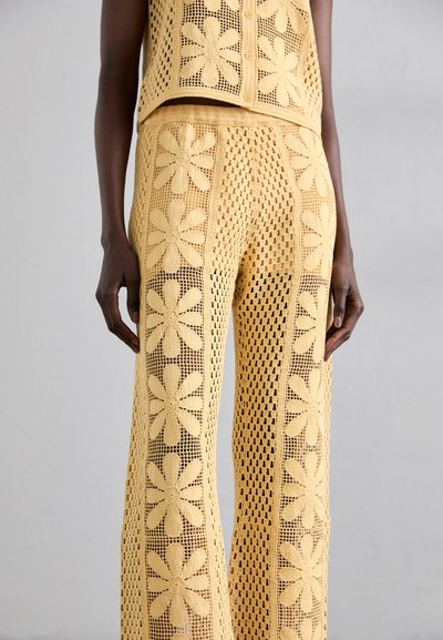 Ensemble en crochet jaune composé de deux pièces, avec des motifs floraux, comprenant un haut court et un pantalon à jambes larges, mettant en valeur un design en maille ouverte et une texture.