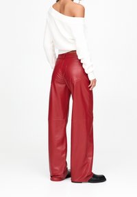 Rode high-waisted faux lederen wijde broek met achterzakken en een gladde textuur, gecombineerd met een witte off-shoulder gebreide trui.