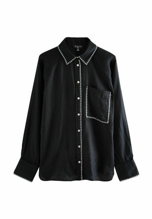 Sort skjorte med lange ærmer og knapper, med hvide zigzag-sømme på kraven, knapstolpen, lommen og manchetterne.