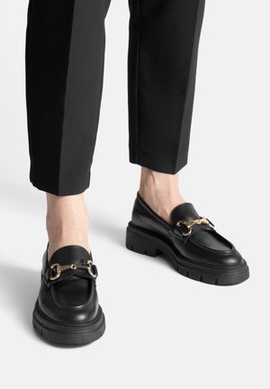 Czarne skórzane mokasyny z masywną podeszwą, ozdobione złotym łańcuszkiem na górze. Gładka tekstura i zaokrąglony nosek.