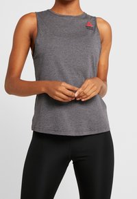 Šedý sportovní top bez rukávů vyrobený z měkké elastické látky; má na rameni červené logo Reebok a kulatý výstřih.