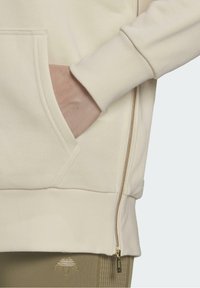 Krämfärgad sweatshirt med dragkedja i sidan, känguruficka och ribbade mudd. Har detaljer i guld och mjuk textur.