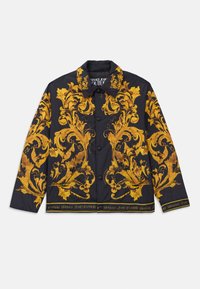 Jachetă neagră cu nasturi, decorate cu modele florale barocie galbene ornate și textul "Versace Jeans Couture" pe marginea tivului și a căptușelii gulerului.