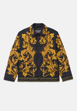 Black button-up jacket with ornate yellow baroque floral patterns and "Versace Jeans Couture" text along the hem and collar lining.