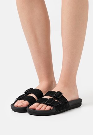 Chanclas negras con dos correas ajustables que cuentan con hebillas, parte superior de tela texturizada y suela de goma plana. Diseño ligero.