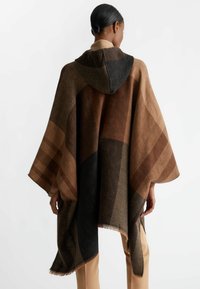 Kapuzenpončo s geometrickým vzorem v odstínech hnědé, černé a pískové, vyrobené z texturované tkaniny s třásněmi.