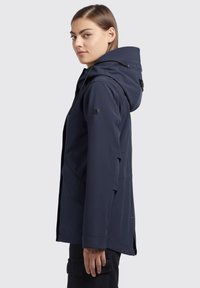 Giacca impermeabile blu navy con cappuccio, dotata di tasche con zip, colletto testurizzato e polsini regolabili, mostrata di lato.