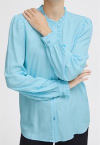 Camicia button-up azzurro chiaro realizzata in tessuto texturizzato, con colletto arricciato e polsini con bottoni, maniche lunghe e vestibilità comoda.