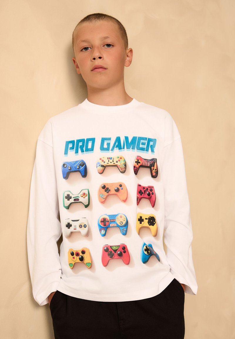 Biała koszula z długim rękawem, zdobiona kolorową grafiką kontrolerów do gier oraz napisem "PRO GAMER" w kolorze niebieskim z przodu. Okrągły dekolt, luźny krój.