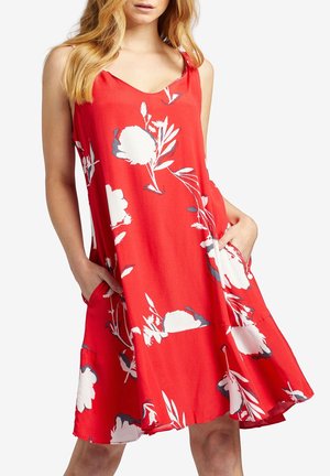 Rød ærmeløs kjole med hvidt blomsterprint, der har sidelommer og en udvidet skørtkant. Fremstillet af et glat, let stof.