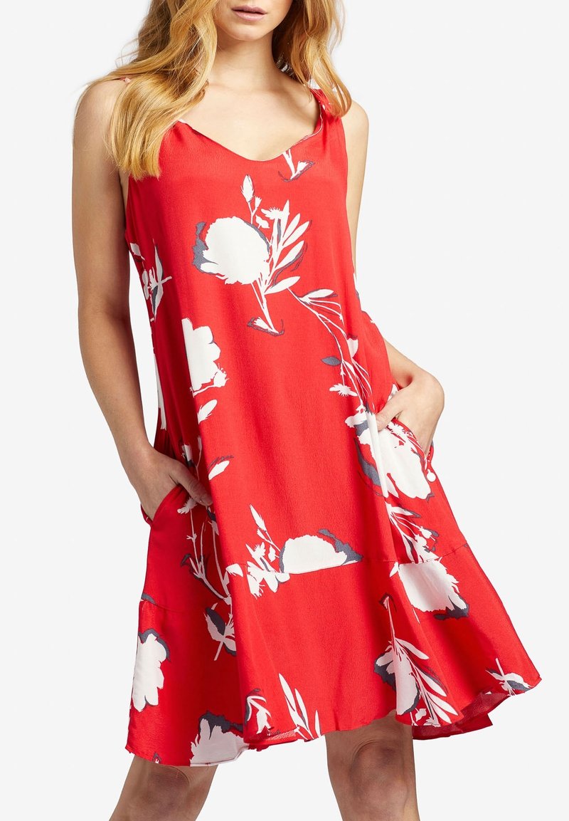 Robe rouge sans manches avec imprimé floral blanc, dotée de poches latérales et d'un ourlet évasé. Fabriquée en tissu lisse et léger.