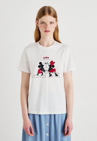 White cotton T-shirt featuring a graphic print of Mickey and Minnie Mouse in black and red. Design includes hearts and the word "SMACK!"