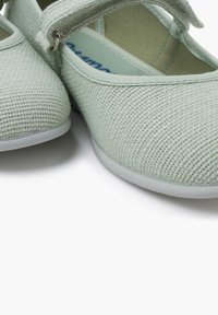 Svetle zelené ploché boty s texturovaným tkaným svrškem, elastickým popruhem a bílou gumovou podrážkou, nabízející jednoduchý design a jemné detaily.