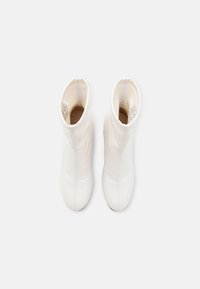 Bottes blanches à chevilles avec une finition lisse et brillante. Design élancé et ajusté avec des détails de couture et un bout arrondi.