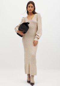 Knitad beige klänning med en figurnära silhuett, ribbat mönster, rundad halsringning och puffärmar. Accessoarer med en svart handväska.
