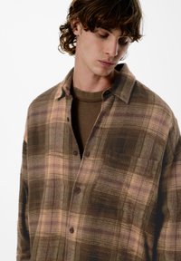 Rjava karirana srajca iz mehkega blaga v odtenkih bež in vijolične barve, z zapiranjem na gumbe in enim žepom na prsih.