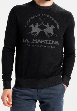 Mann trägt einen schwarzen Pullover mit der Aufschrift "La Martina Buenos Aires" und einem grauen Polospieler-Logo auf der Brust.