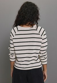 Pullover neule, jossa on mustavalkoiset vaakaraitat, pehmeä neulepinta, raglan-hihat ja pyöreä pääntie.
