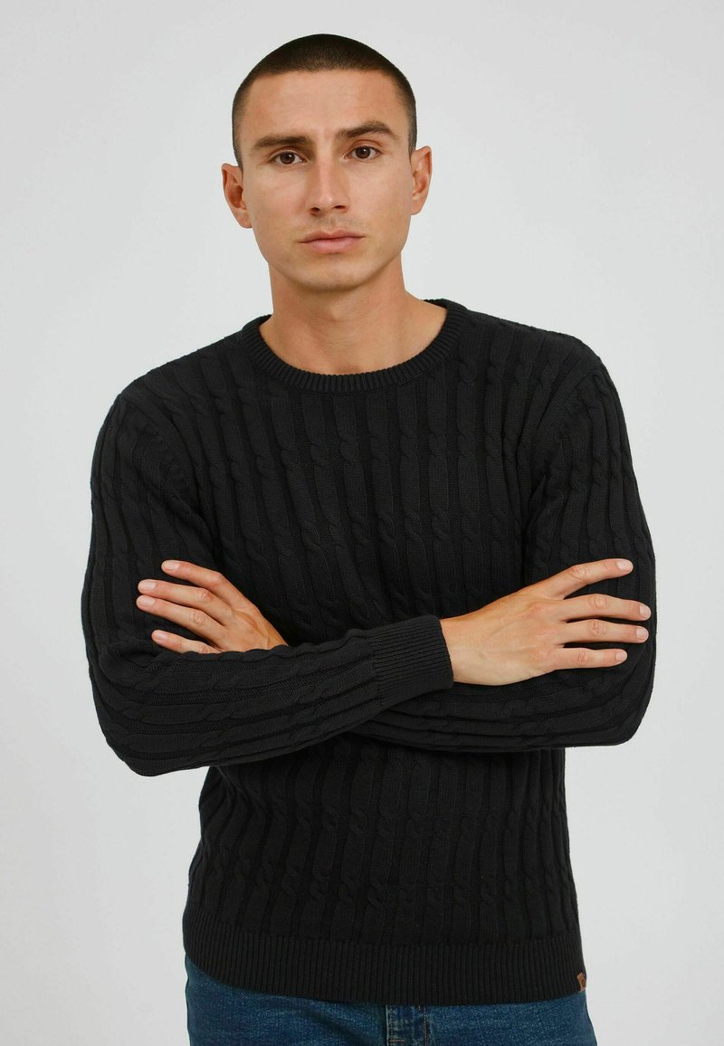 Pull noir en maille torsadée à manches longues et col rond. Poignets et ourlet côtelés, avec un motif texturé. Coupe décontractée.