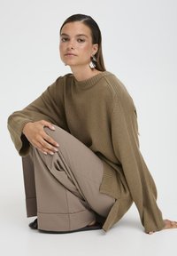 Suéter marrón de gran tamaño con detalles acanalados, combinado con pantalones beige de pierna ancha. El suéter cuenta con un escote redondo y hombros caídos.