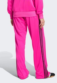 Rosa sportieve broek heeft een losse pasvorm, een gladde textuur en zwarte zijstrepen. De tailleband is elastisch voor comfort en ondersteuning.