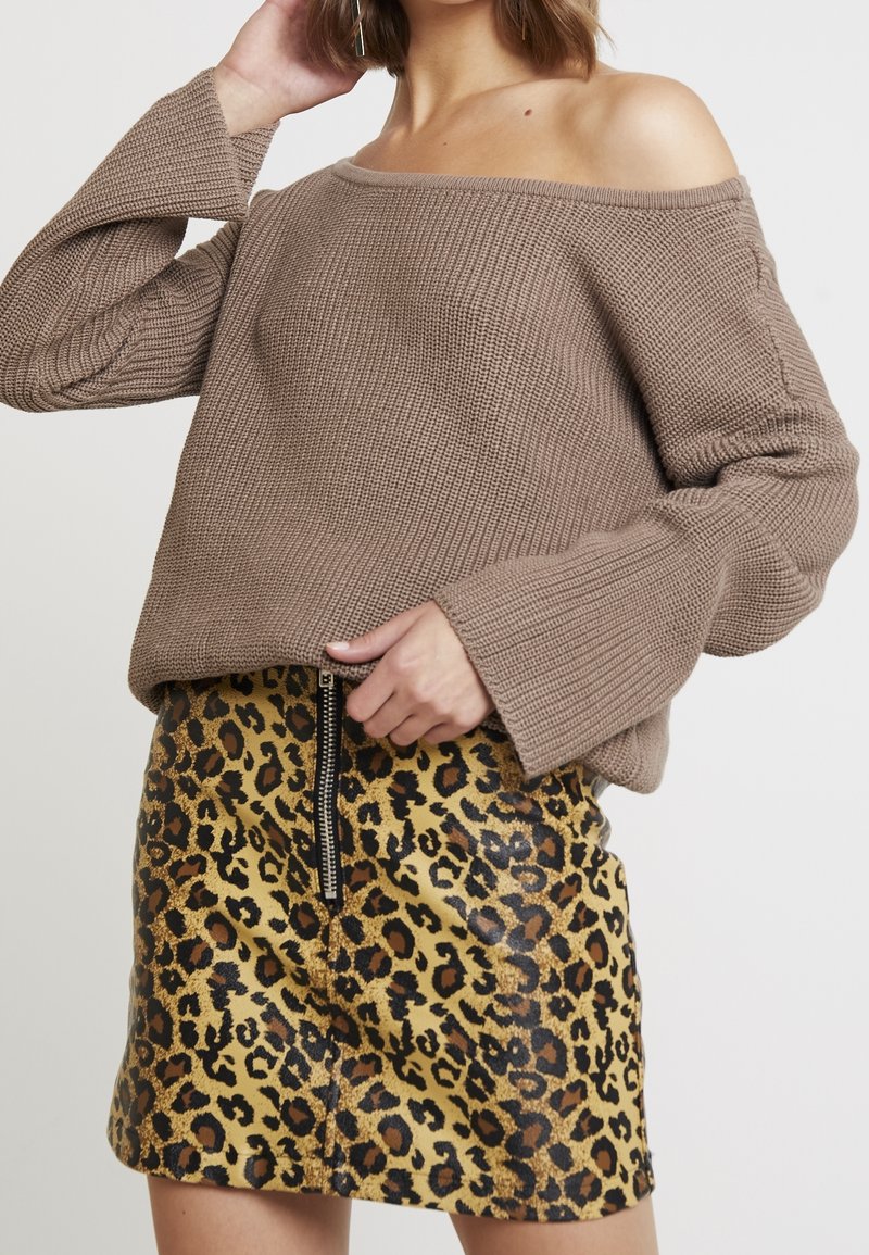 Hnědý pletený svetr s off-shoulder designem a žebrovanou strukturou, kombinovaný se žlutou sukní z umělé kůže s leopardím vzorem a detaily na zip.