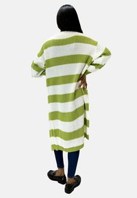 Randig kofta i grönt och vitt, stickad material, långa ärmar, öppen front, knälång, i kombination med mörka jeans och svarta skor.