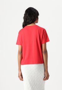 Red cotton t-shirt with short sleeves and a round neckline, viewed from the back. Features a straight cut and casual fit.