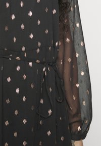 Μαύρο φόρεμα με σφιχτή μέση, διαθέτοντας λεπτομέρεια με βά ties και διάφανες μανίκες. Διακοσμημέν�ο με μοτίβα ροζ χρυσού σε όλη την επιφάνεια.