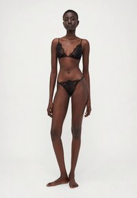 Conjunto de lencería de encaje negro que incluye un sujetador con tirantes ajustables y un tanga a juego, que muestra intrincados patrones florales y una textura transparente.