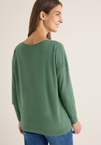 Maglione verde a maglia con scollo ampio, vestibilità rilassata e orlo a coste. La trama è liscia e ha maniche lunghe, leggermente scese.