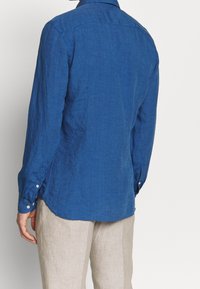 Camicia in lino blu con maniche lunghe, polsini a bottone e orlo curvo. Sottile texture e design pulito e semplice.