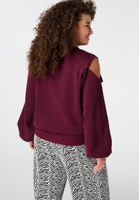 Sweatshirt bordeaux avec découpes aux épaules, poignets et ourlet côtelés. Associé à un pantalon à motif zèbre noir et blanc.