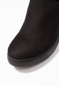 Bottine en daim noir avec un bout arrondi, dotée d'une semelle en caoutchouc texturée et d'un design minimaliste. Surface lisse sans éléments métalliques visibles.