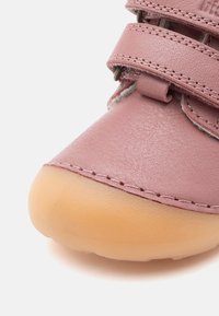 Rosa Lederschuh mit zwei Klettverschlüssen, abgerundeter Form und Gummisohle. Glatte Oberfläche mit feinen Nähten entlang der Kanten.