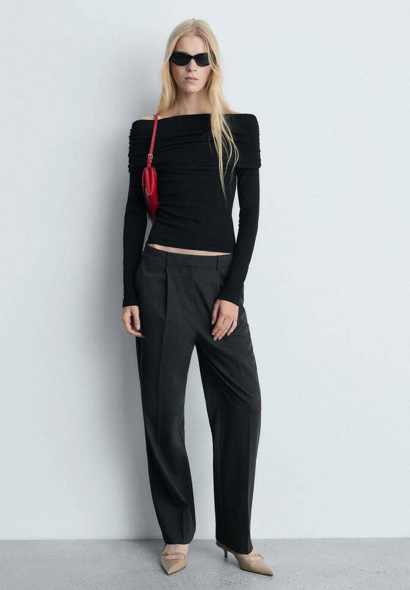 Schwarzes Off-Shoulder-Oberteil mit langen Ärmeln und gerafften Details, kombiniert mit grauen hochtaillierten Hosen und beigen spitzen Absatzschuhen. Rote Tasche inklusive.