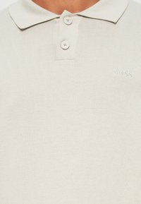 Polo claro bege feito de tecido de malha texturizado, com um fecho de dois botões e pequeno logótipo bordado "BOSS" no peito.